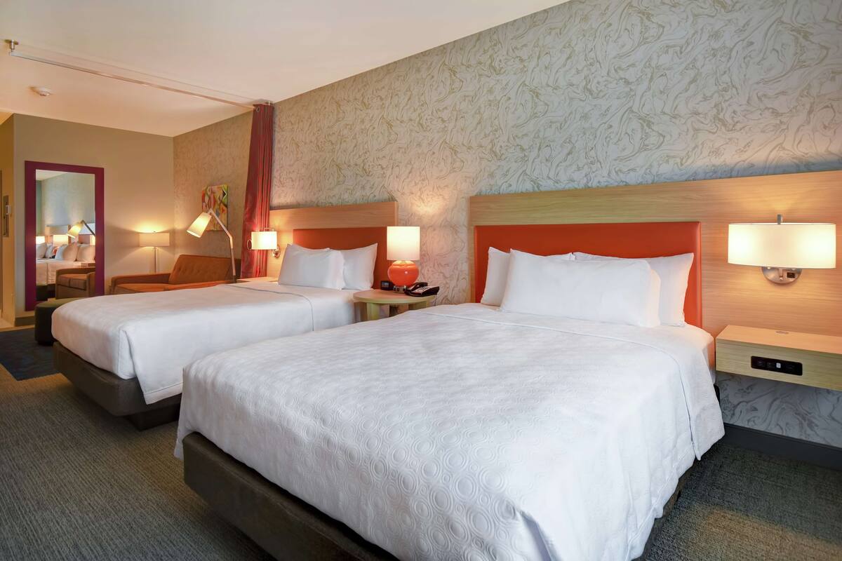 Ein Hotelzimmer mit zwei Betten, einem Spiegel, einem kleinen Tisch und einer Lampe.