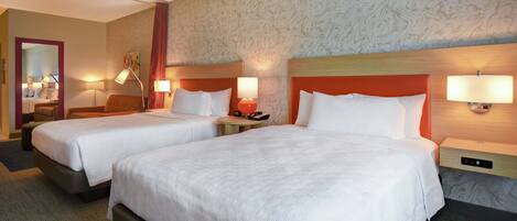 A hotel room with two beds, a mirror, a small table, and a lamp.