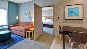 Una habitación de hotel con sofá, una mesita, una mesa de comedor con sillas, una cama y un cuadro en la pared.