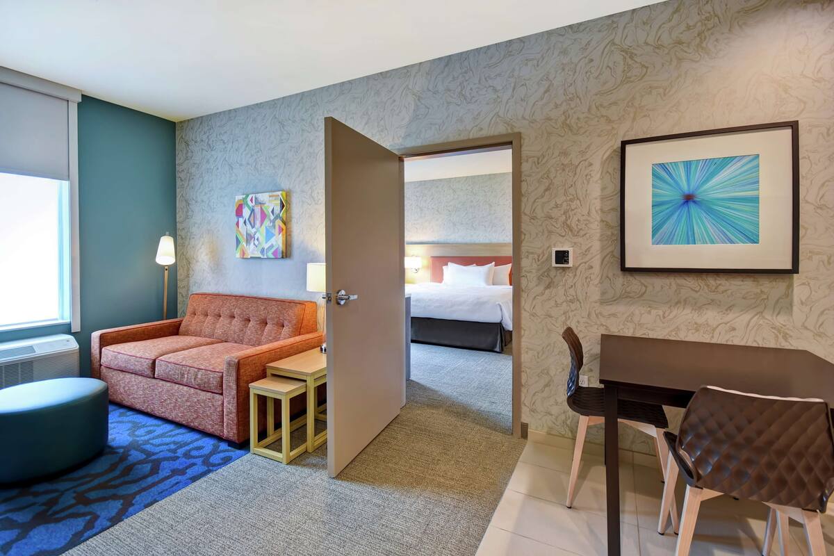 Ein Hotelzimmer mit einer Couch, einem kleinen Tisch, einem Esstisch mit Stühlen, einem Bett und einem Bild an der Wand.