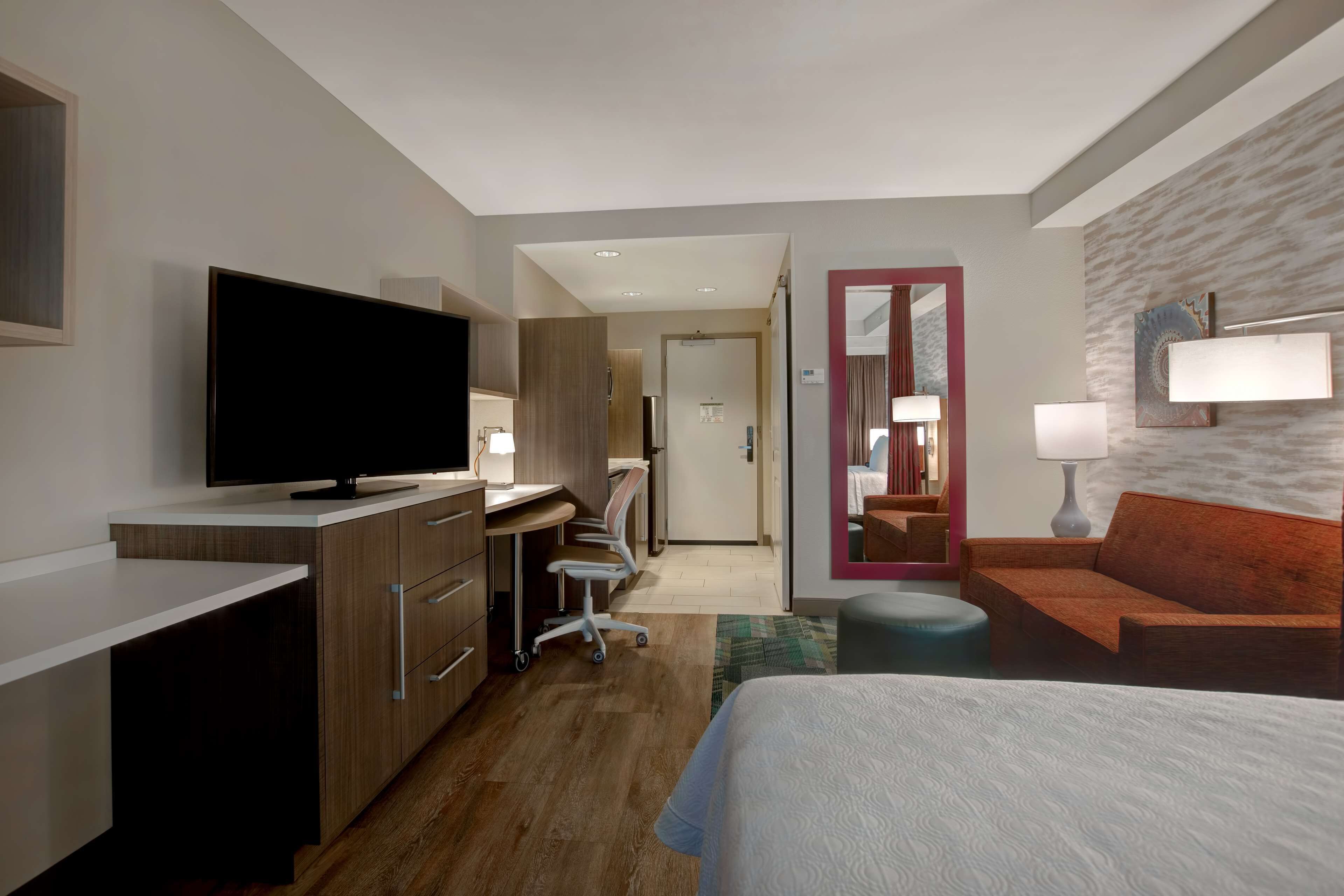 Quarto de hotel com uma cama, uma escrivaninha com televisão de tela plana, uma cadeira, um sofá e um espelho.