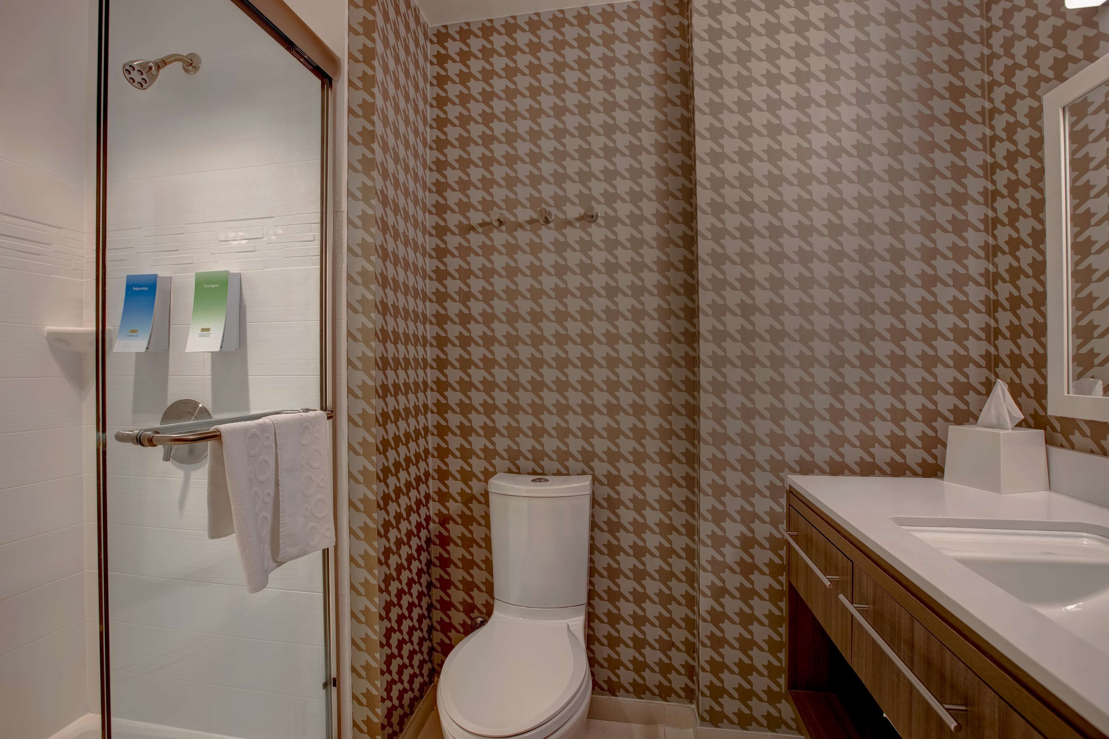 A bathroom with a patterned wall, a toilet, a sink, and a glass shower enclosure.