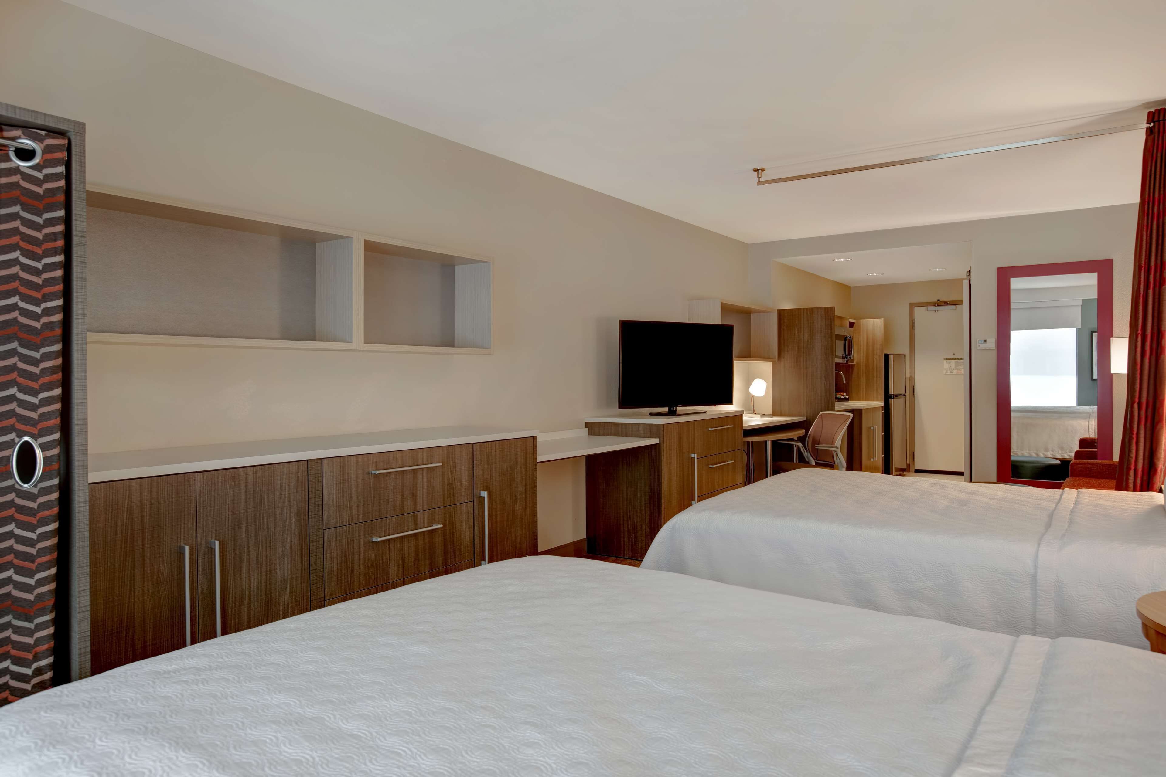 A hotel room with two beds, a desk with a television, and a bathroom visible through an open door.