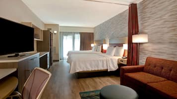 A hotel room with a bed, a desk with a TV, a sofa, and a chair.