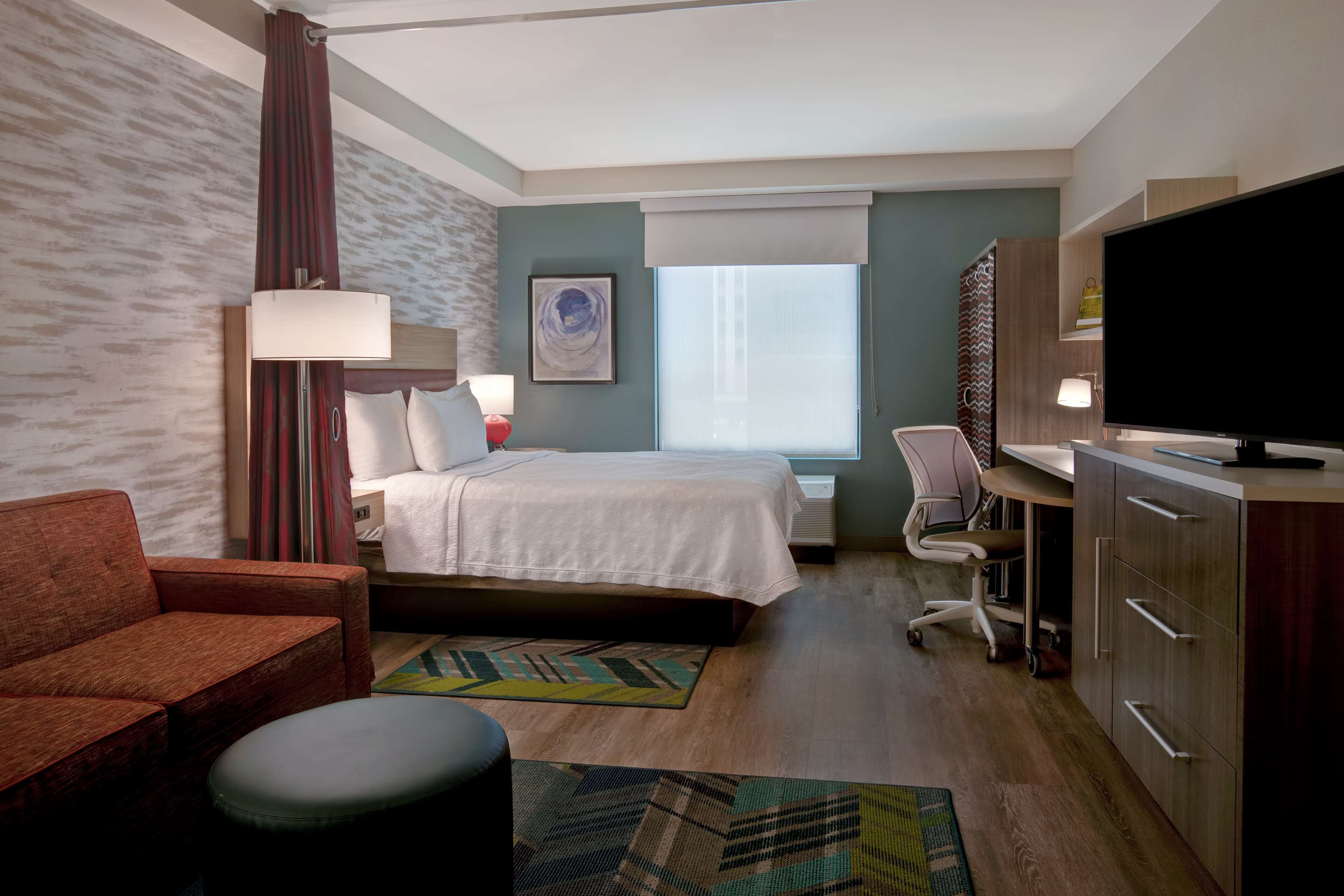 A hotel room with a bed, a desk, a chair, a TV, and a sofa.
