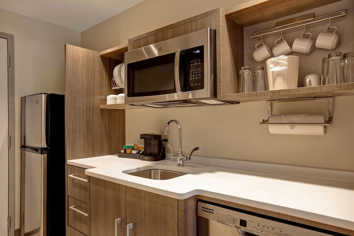 Eine moderne Küche mit einem Edelstahl-Kühlschrank, einer Mikrowelle, einer Kaffeemaschine und einem Geschirrspüler.