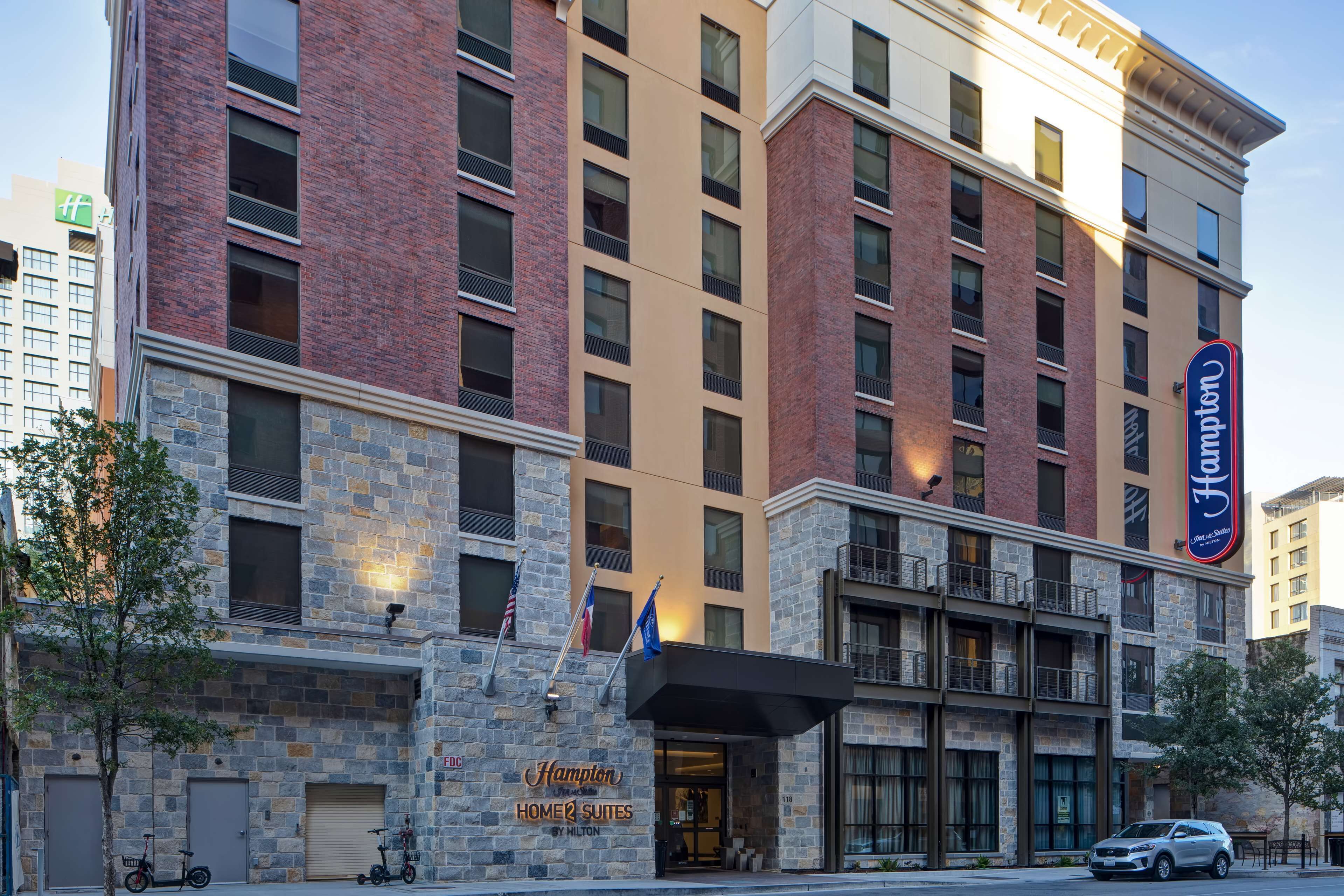 Un hotel con fachada de piedra, varios balcones y un cartel de Hampton Home 2 Suites by Hilton.