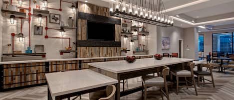 A modern dining area with a long table, chairs, and a chandelier.