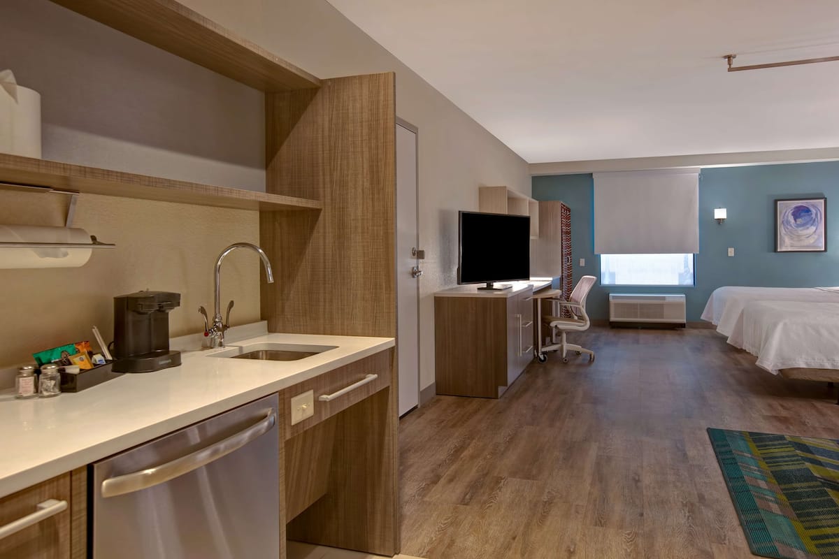 Ein modernes Hotelzimmer mit Küchenzeile, Flachbildfernseher, Schreibtisch und Bett.