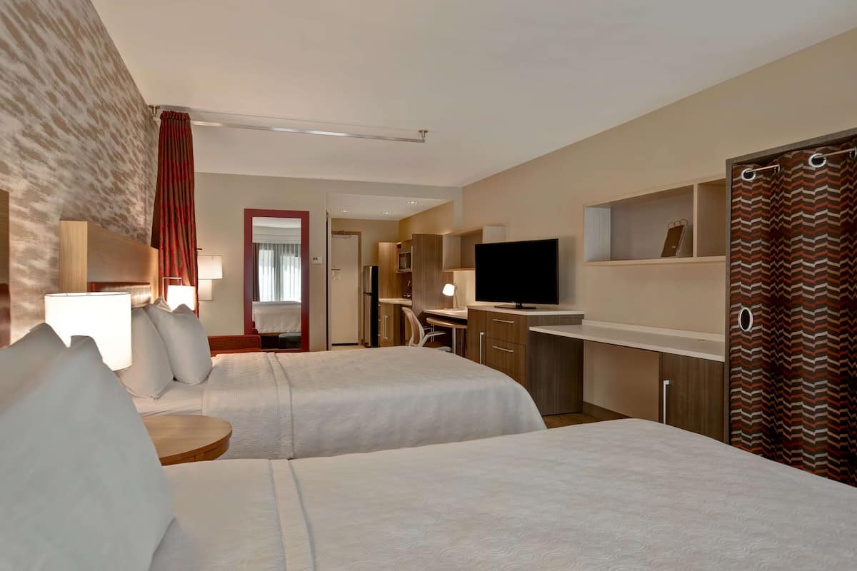 Ein Hotelzimmer mit zwei Betten, einem Schreibtisch, einem Fernseher und einem Kleiderschrank.