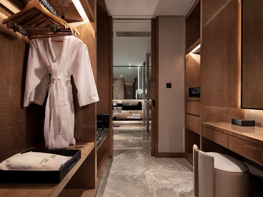 A modern hotel bathroom with a wooden vanity, a robe hanging on a rack, and a mirror.