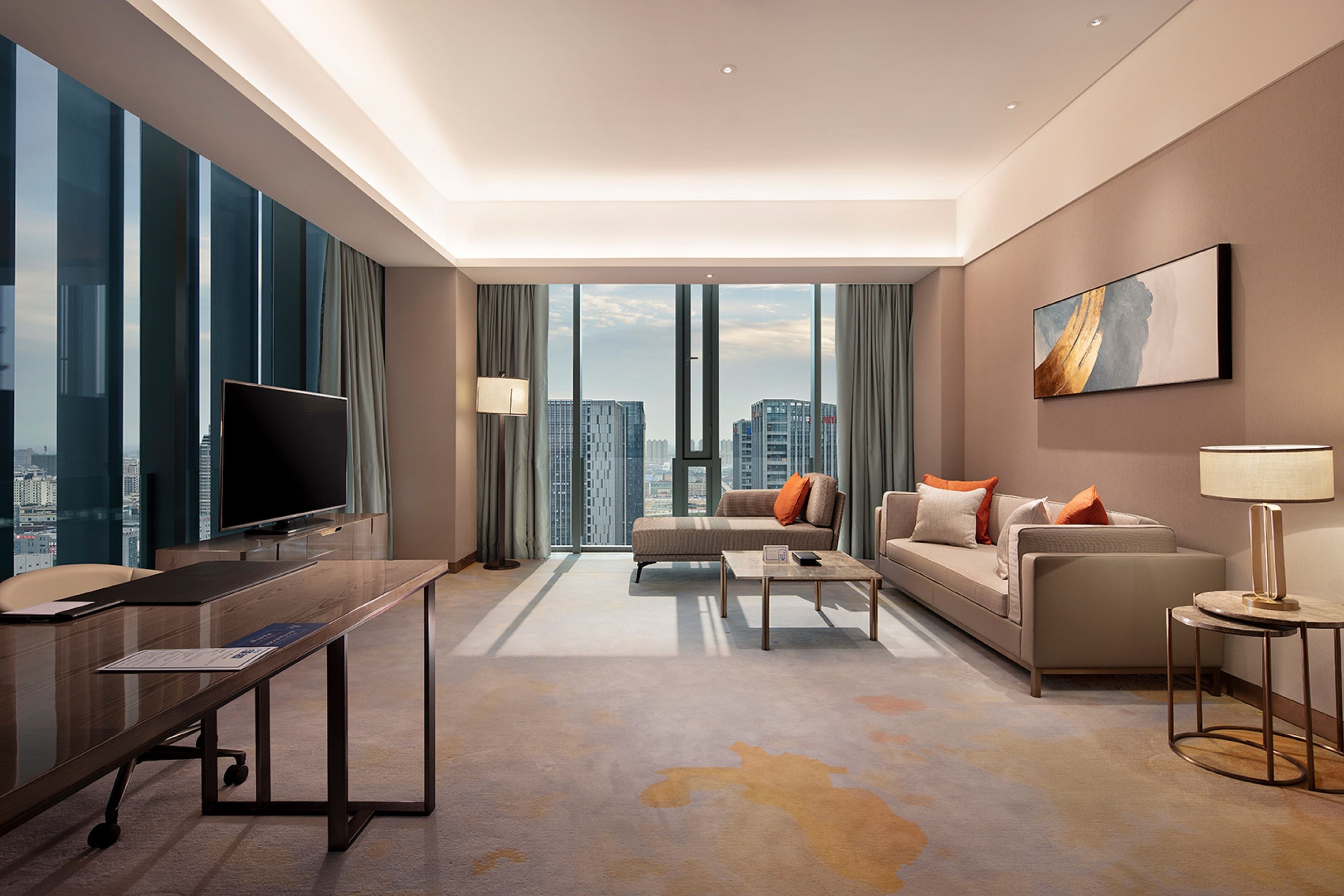A modern hotel room with a large flat-screen TV, a sofa, a coffee table, and a desk with a computer.