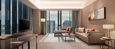 A modern hotel room with a large flat-screen TV, a sofa, a coffee table, and a desk with a computer.