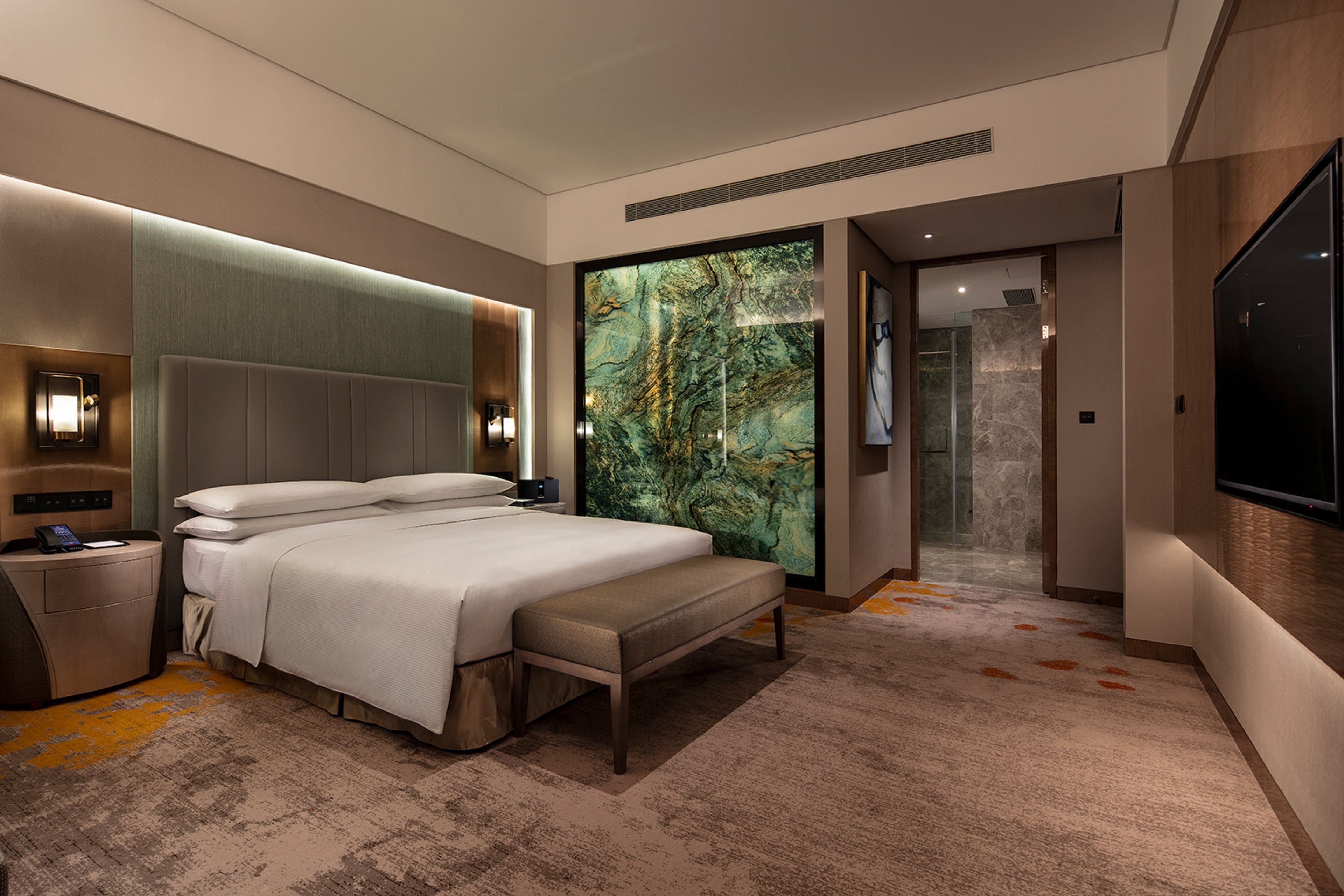 A modern hotel room with a large bed, a bench, a nightstand, a TV, and a large wall mural.