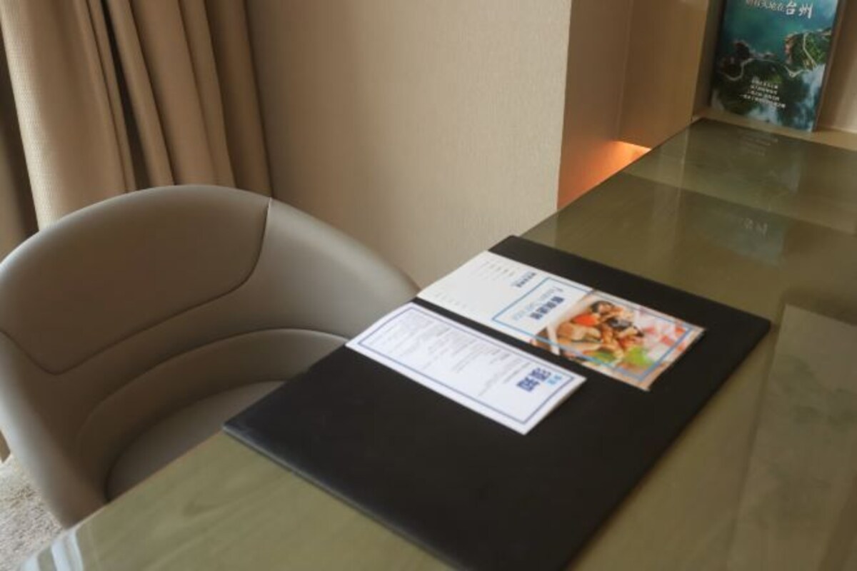 Una habitación de hotel con una mesa de vidrio, una carpeta negra y un cartel en la pared.