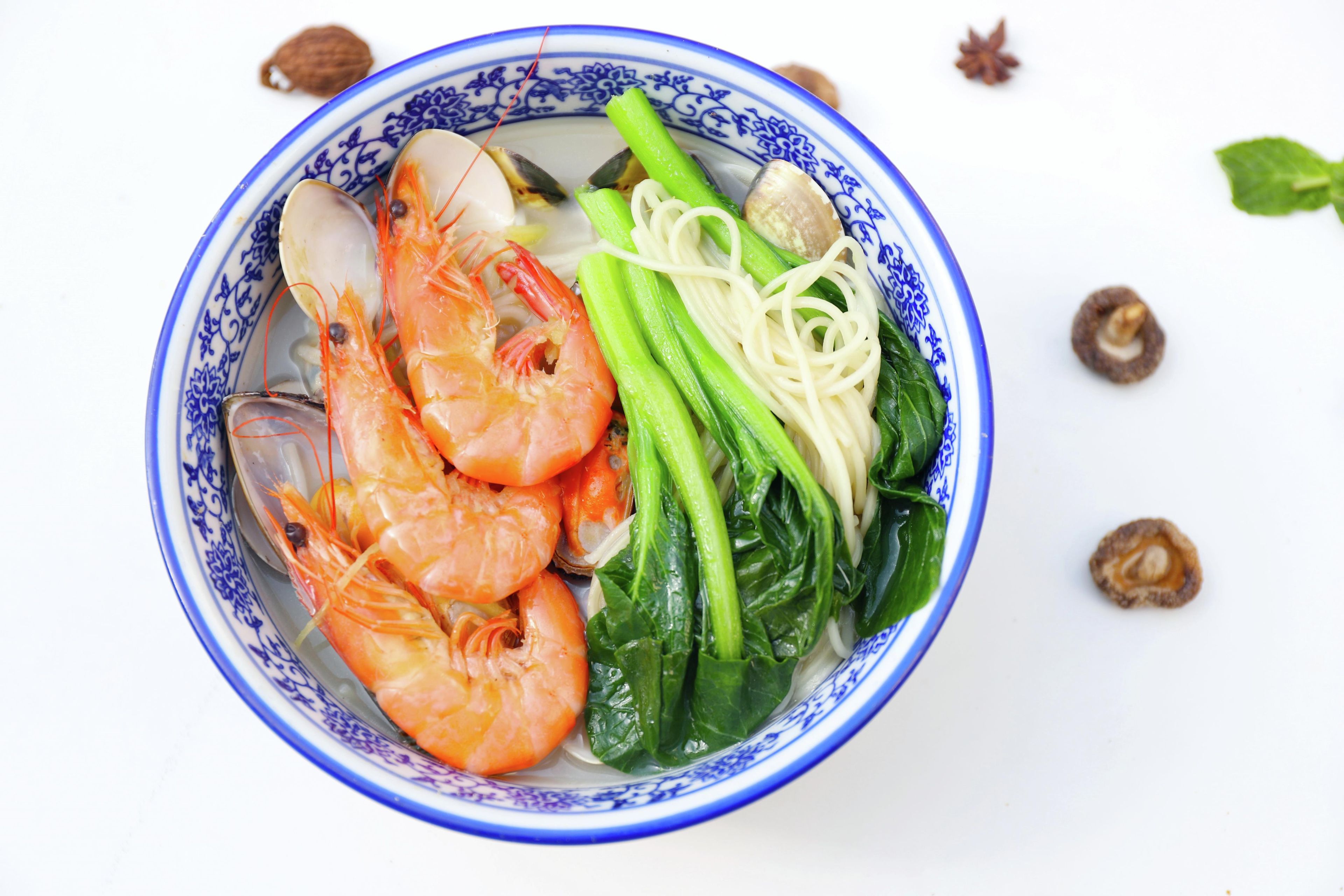 A bowl of soup with shrimp, noodles, and greens.