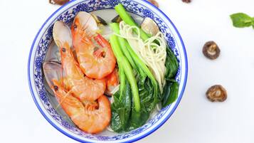 A bowl of soup with shrimp, noodles, and greens.
