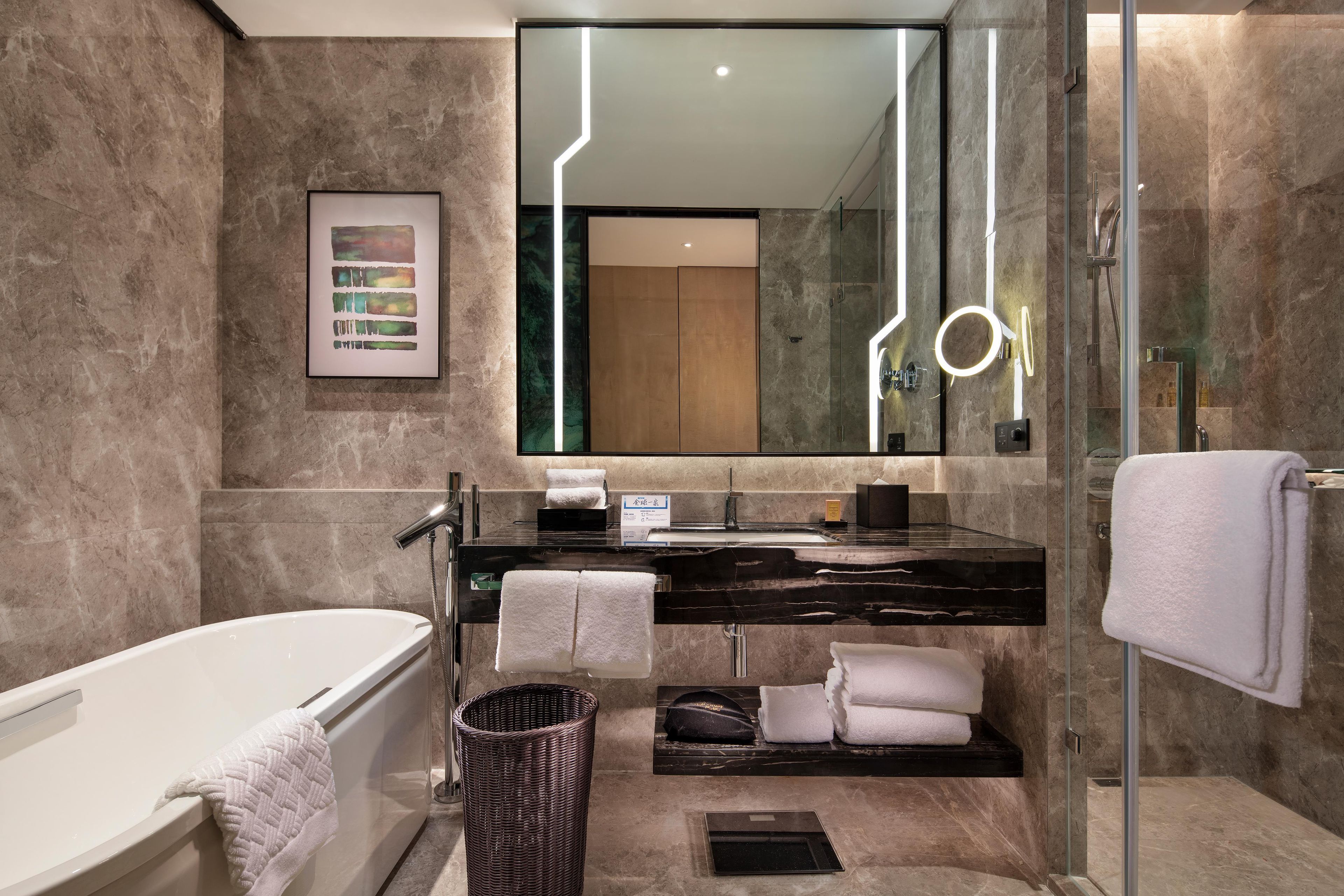 Un baño moderno con bañera, ducha con mampara de vidrio, tocador con espejo y un cuadro en la pared.