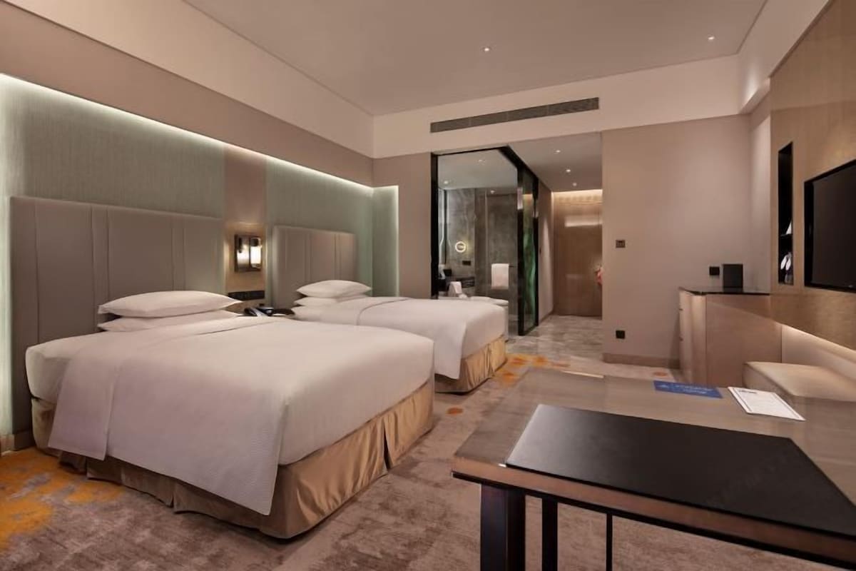 A hotel room with two beds, a desk, and a mirror.