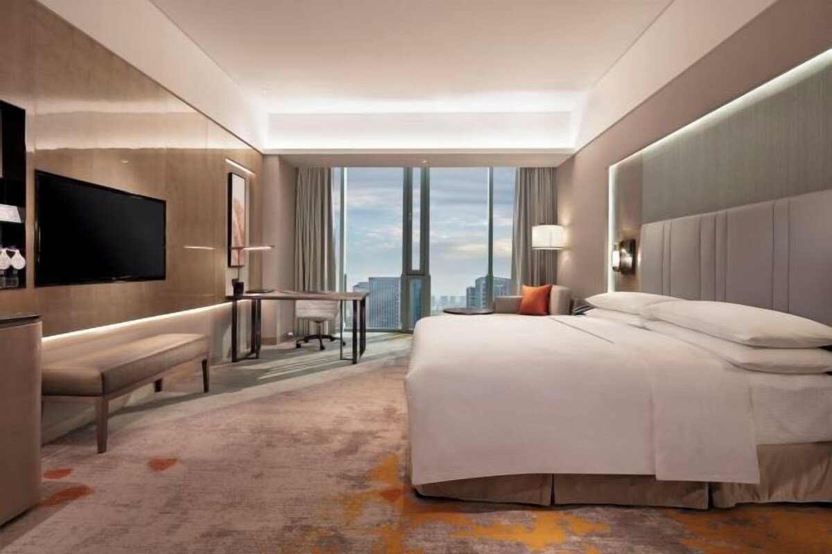 Habitación de hotel con una cama grande, un escritorio, un televisor de pantalla plana y vista a la ciudad.