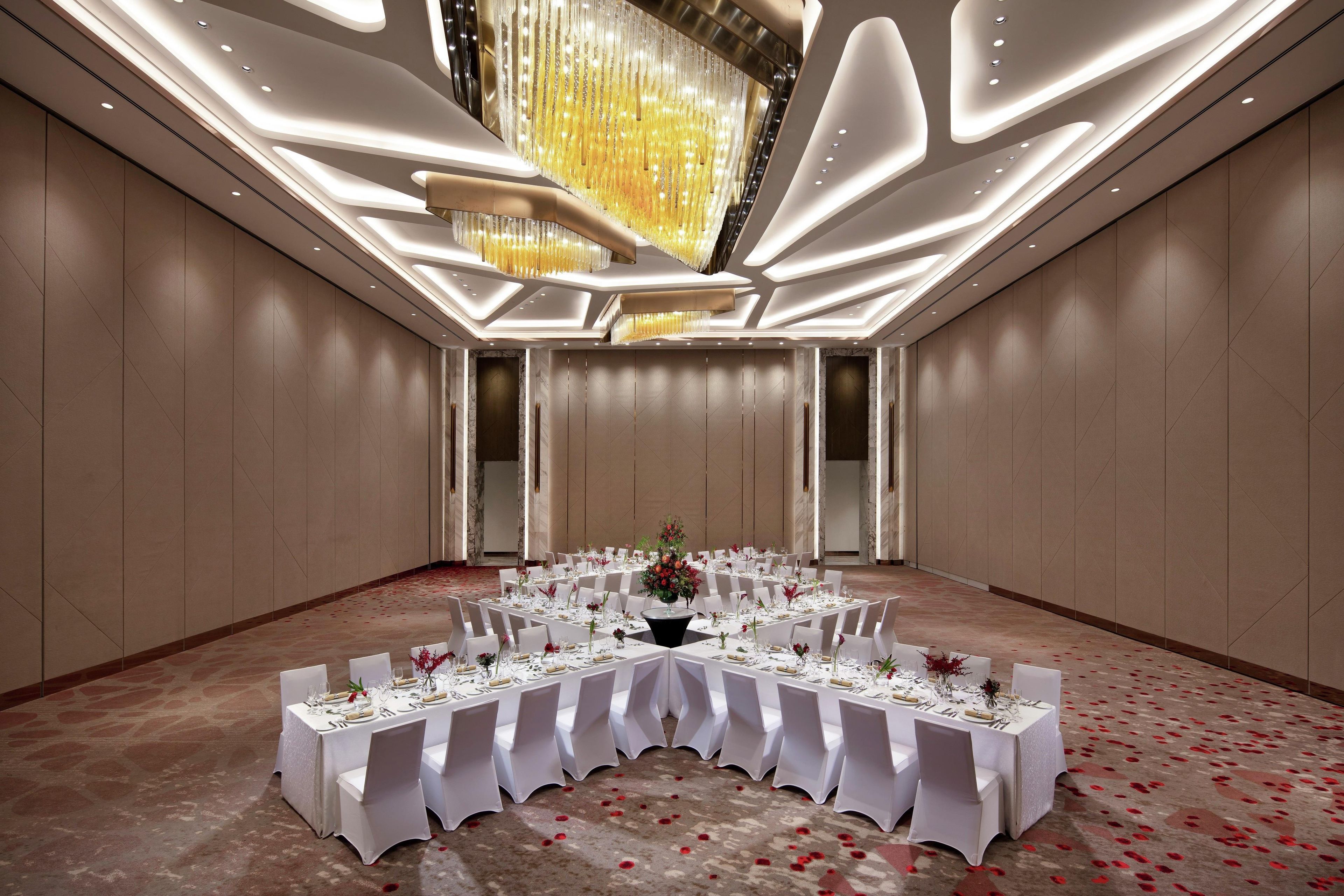 A banquet hall with a long table set for a formal event, featuring a chandelier and a marble wall.