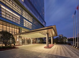 Una entrada de hotel moderna con un vestíbulo cubierto, fachada de vidrio y zona ajardinada.