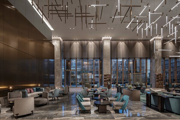 A spacious lobby with modern furniture, large windows, and a high ceiling with hanging lights. - Hilton Taizhou (Taizhou)
