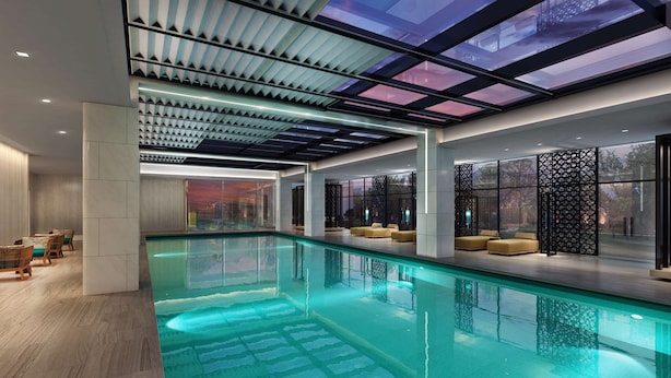 Un área de piscina interior moderna con techo de cristal, zonas de estar y vistas al exterior.