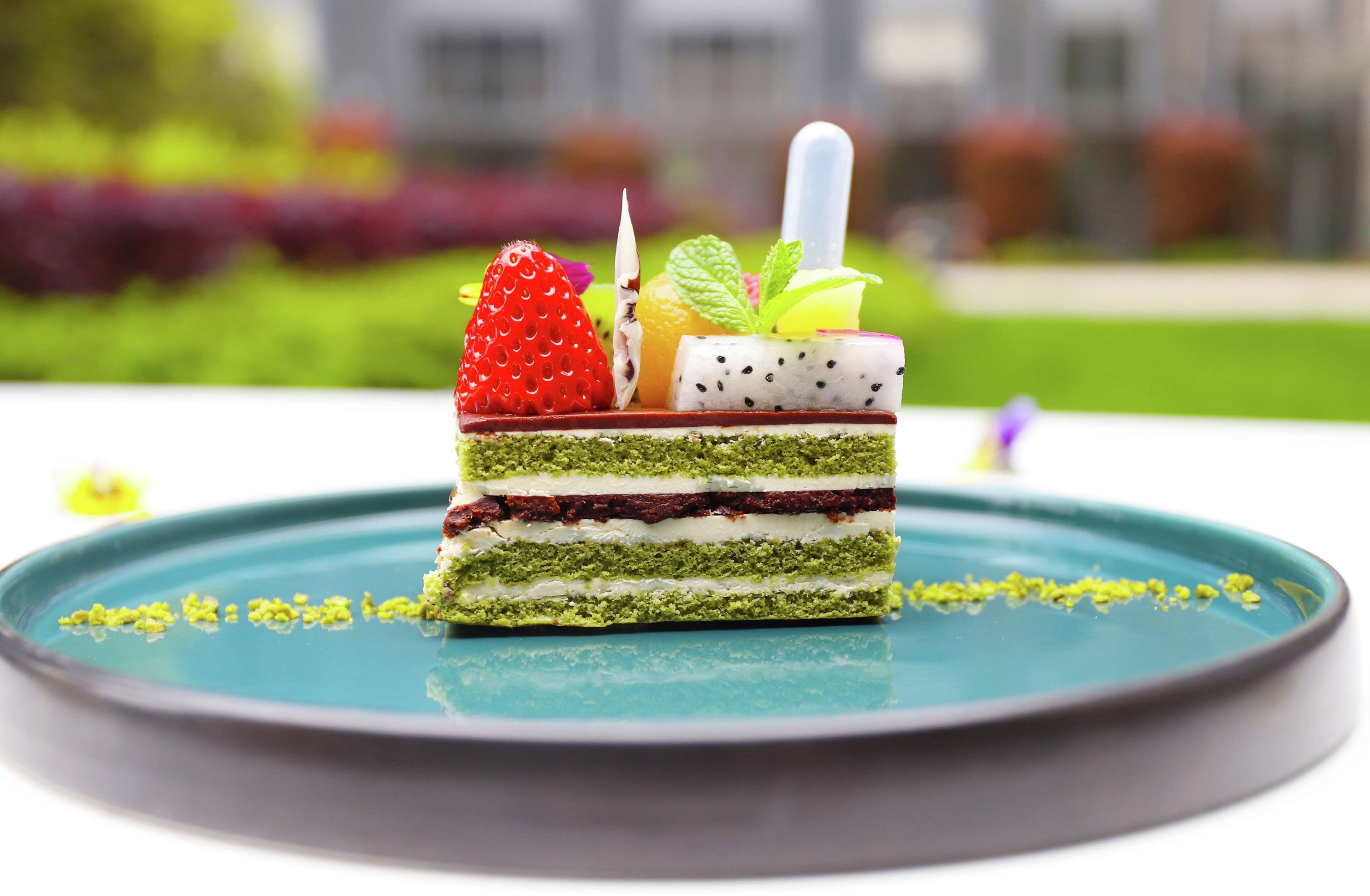 Una porción de pastel en capas con diversas frutas y hojas de menta sobre un plato azul turquesa.