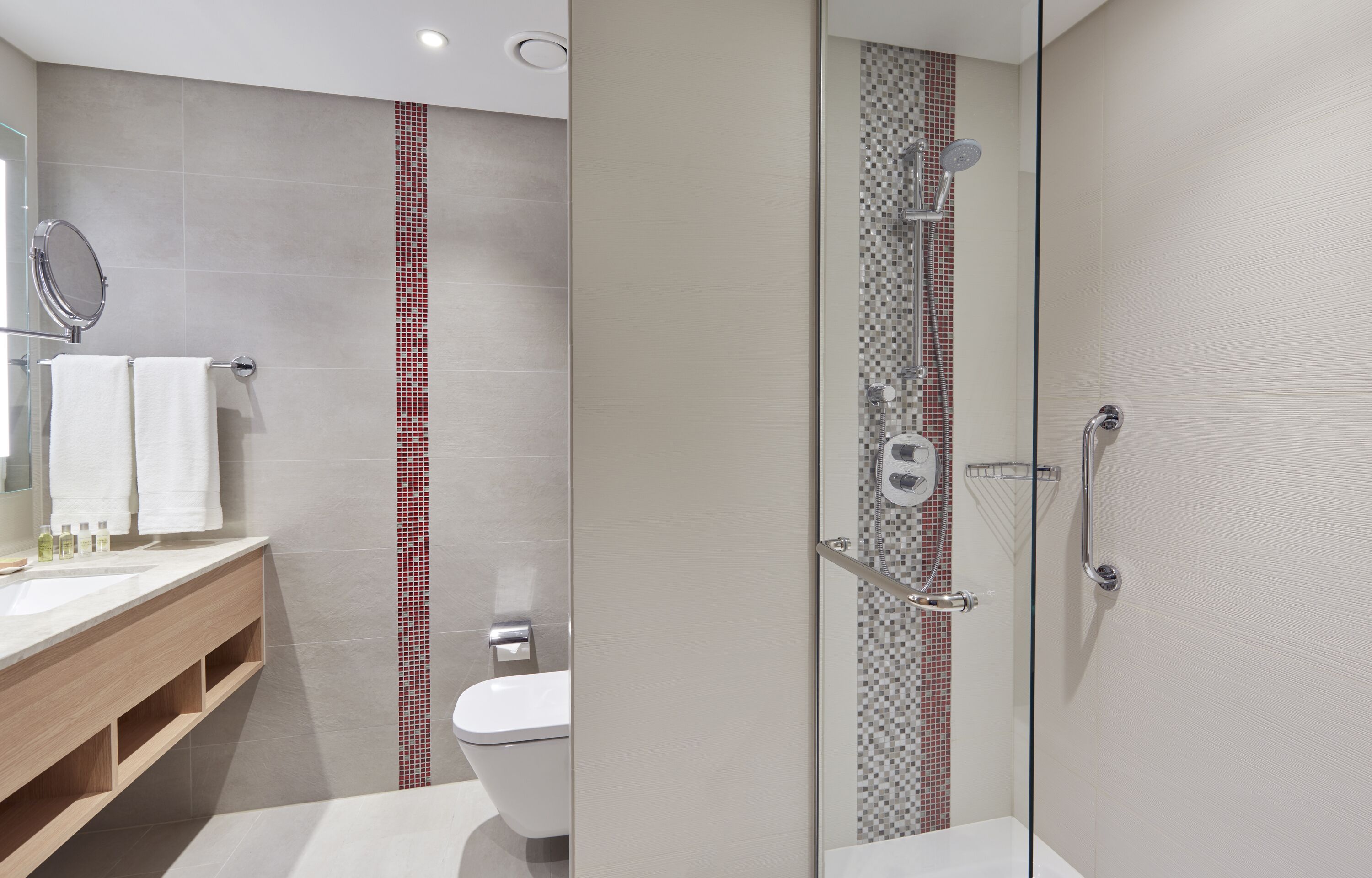 Een moderne badkamer met een douchecabine van glas, een houten wastafelmeubel en een toilet.