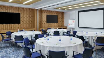 A conference room with multiple round tables, blue chairs, and a large screen.