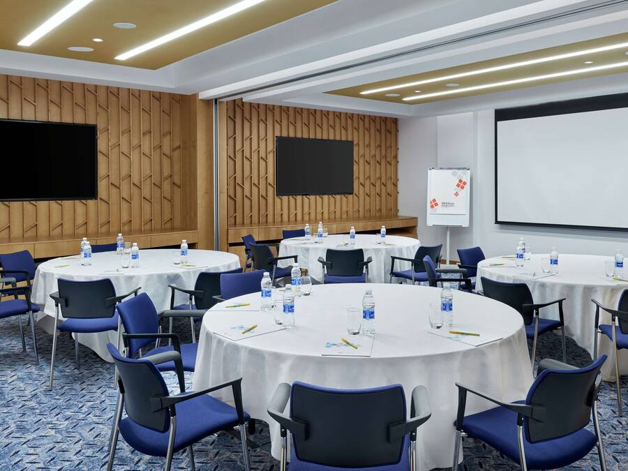 A conference room with multiple round tables, blue chairs, and a large screen.