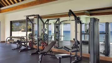 Un gimnasio con equipo de levantamiento de pesas, una prensa de banca y vistas al océano a través de amplios ventanales.
