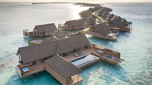 Villas sobre el agua con techos de paja, pasarelas de madera y una piscina central.