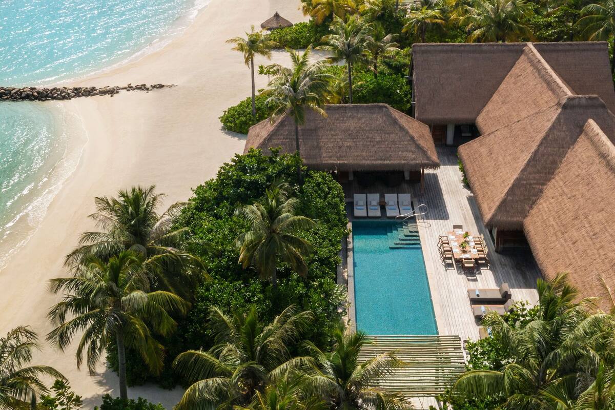 A resort with a pool, thatched-roof buildings, and a beach view.