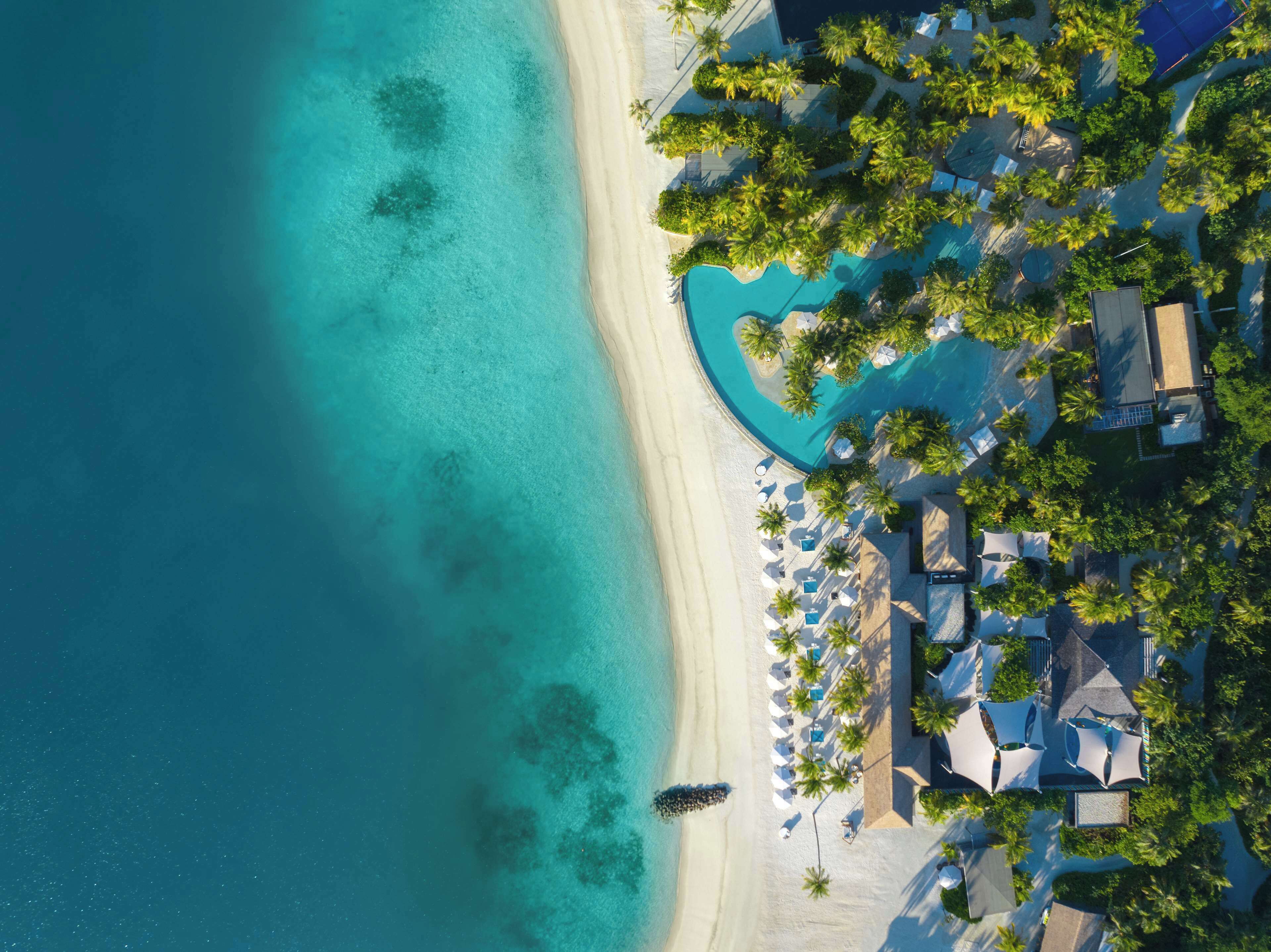 An aerial view of a resort with a beach, a pool, and palm trees.