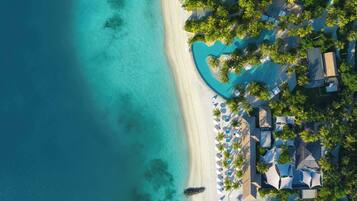 An aerial view of a resort with a beach, a pool, and palm trees.