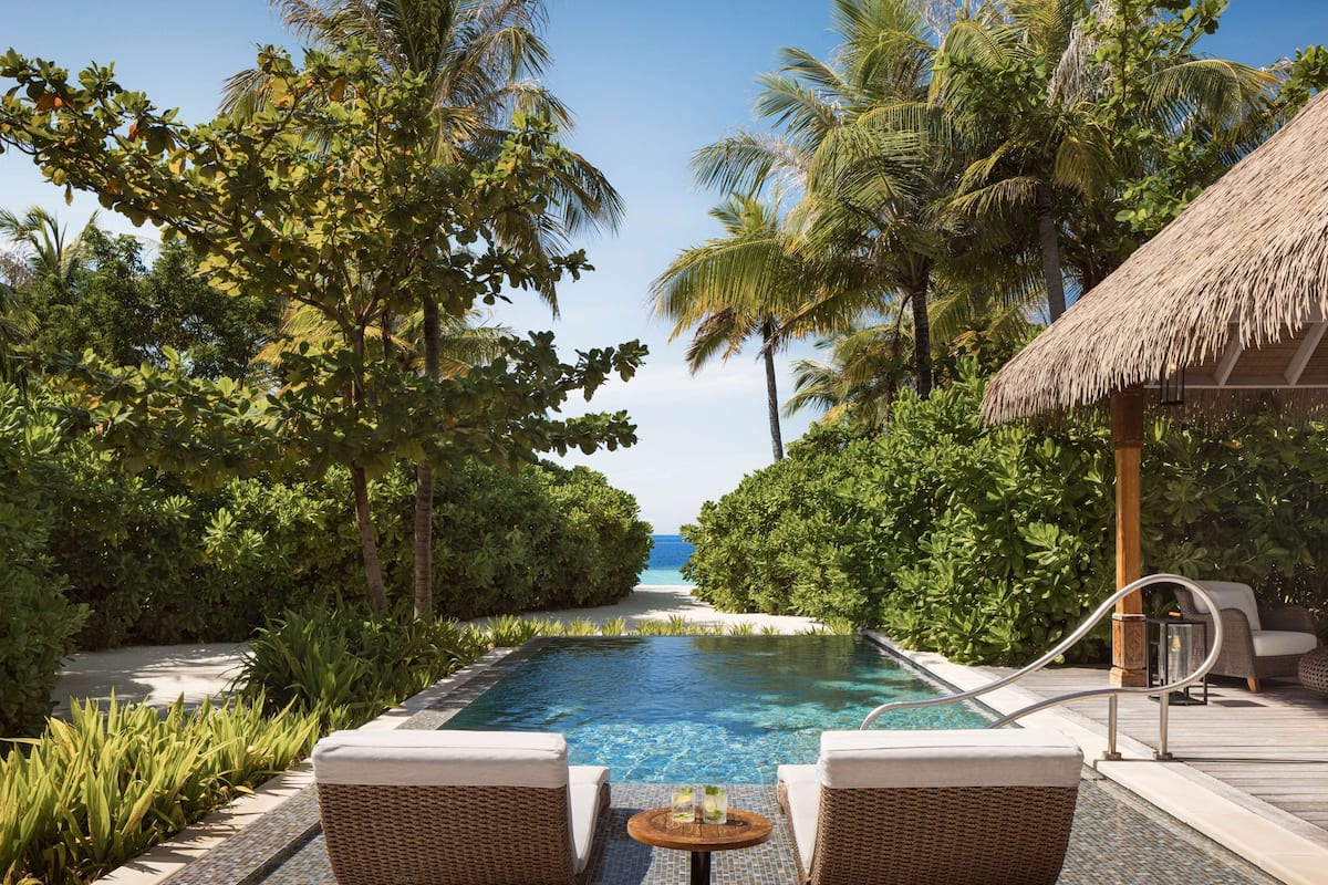 A poolside area with lounge chairs, a thatched-roof structure, and a view of the ocean.