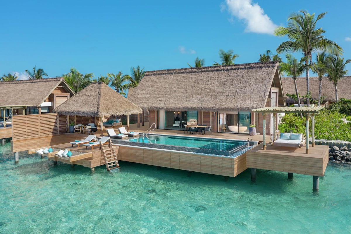 Overwater bungalows with thatched roofs, a pool, and lounge areas.