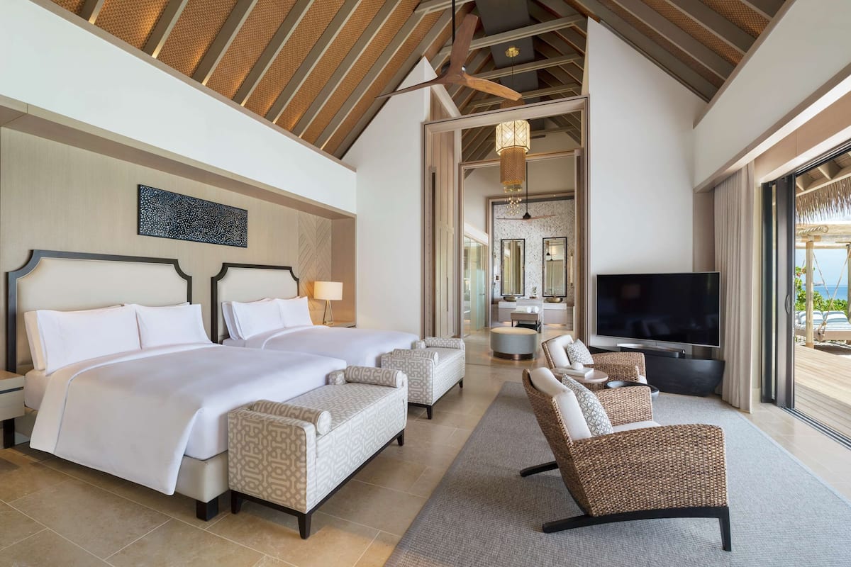 A spacious bedroom with two large beds, a TV, and a balcony with a view.