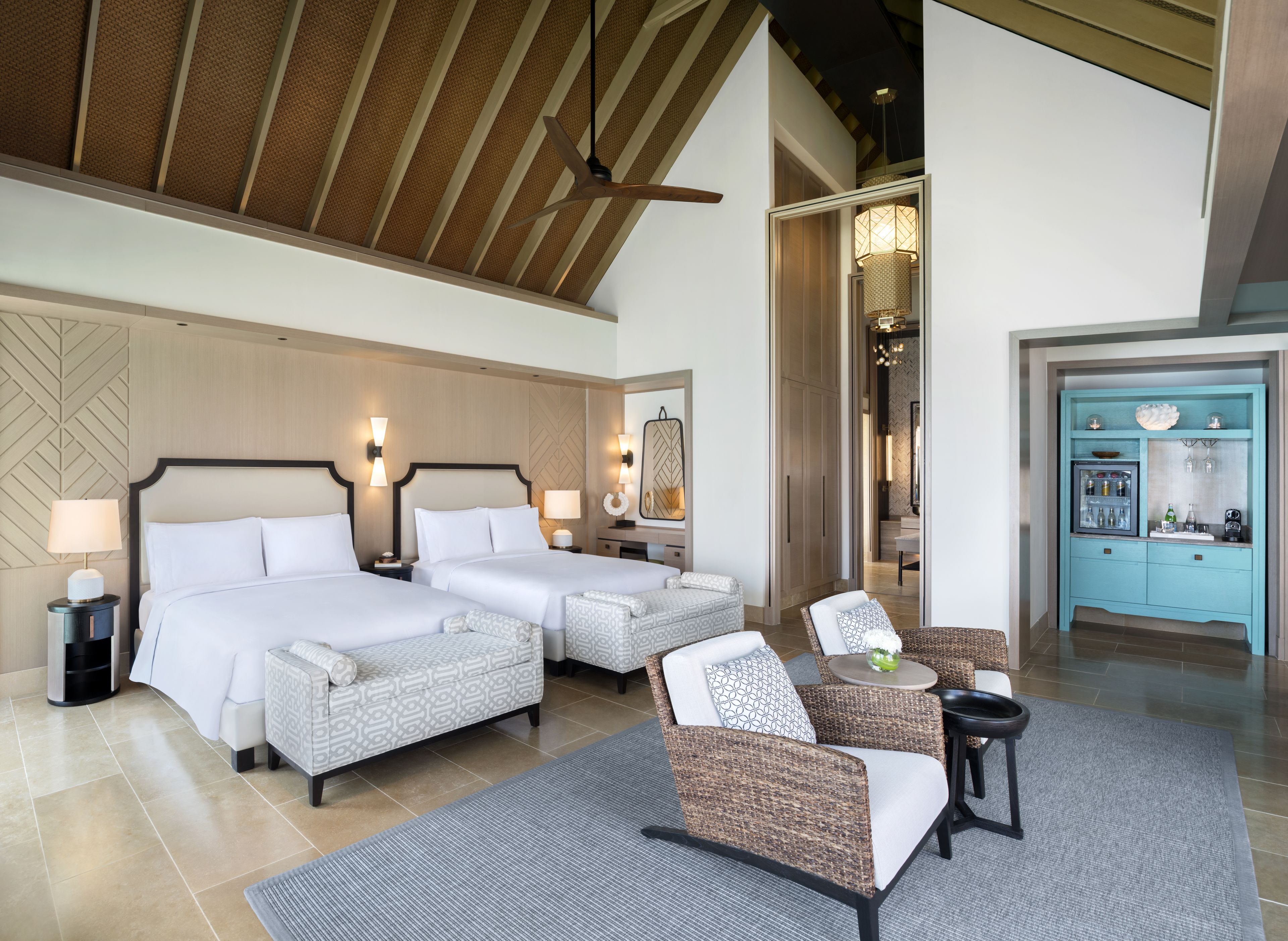 Een hotelkamer met twee bedden, een zithoek met stoelen, een tafeltje en een kitchenette.