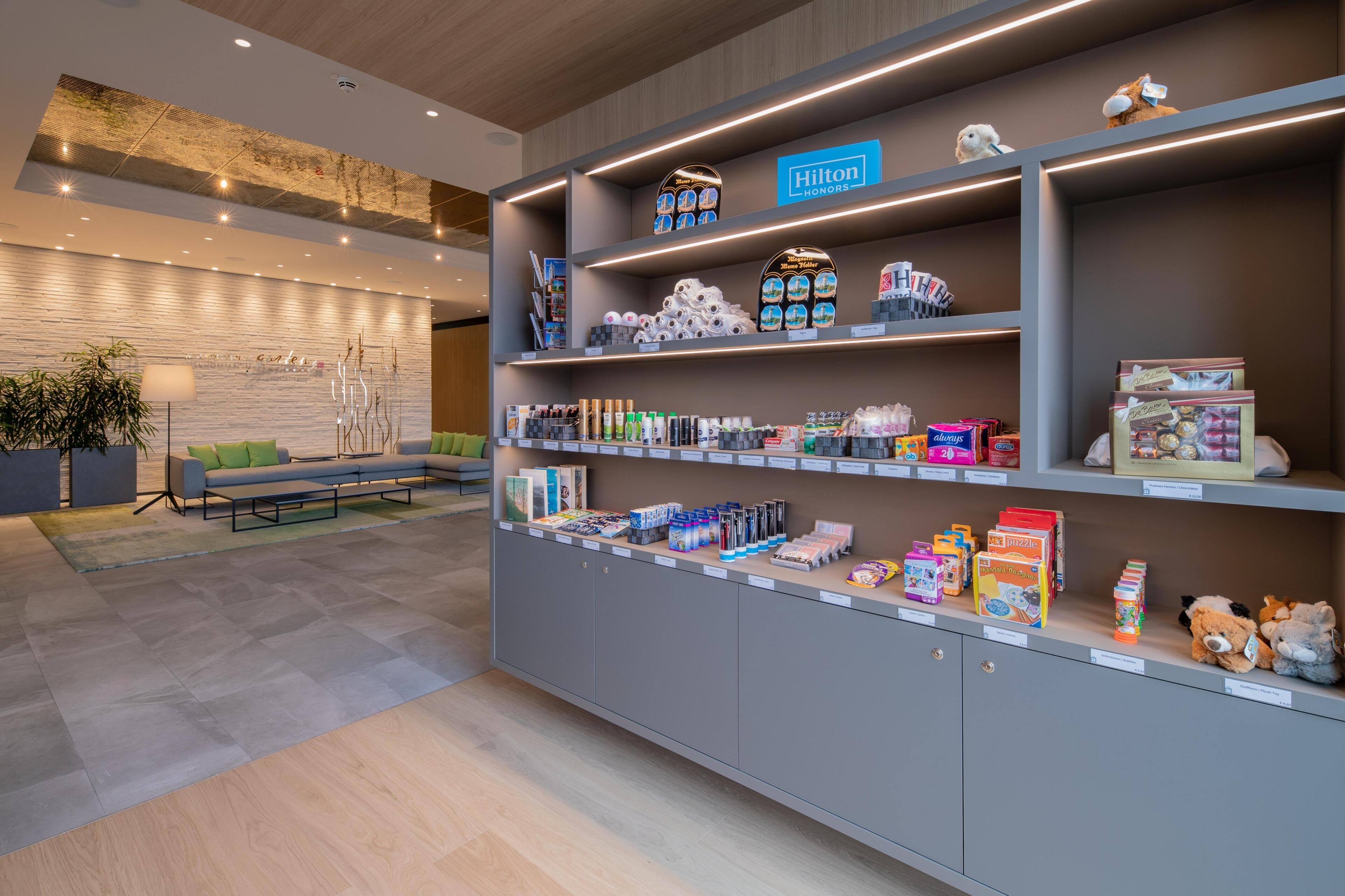 A hotel lobby with a reception desk, seating area, and shelves displaying various items.