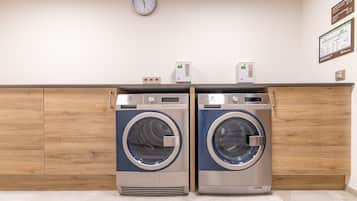 A laundry area with two front-loading washing machines, a clock, and a wall-mounted control panel.