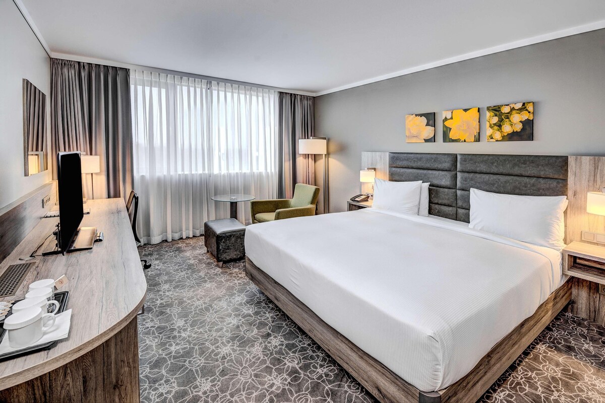 A hotel room with a large bed, a desk with a computer, a chair, and a TV.