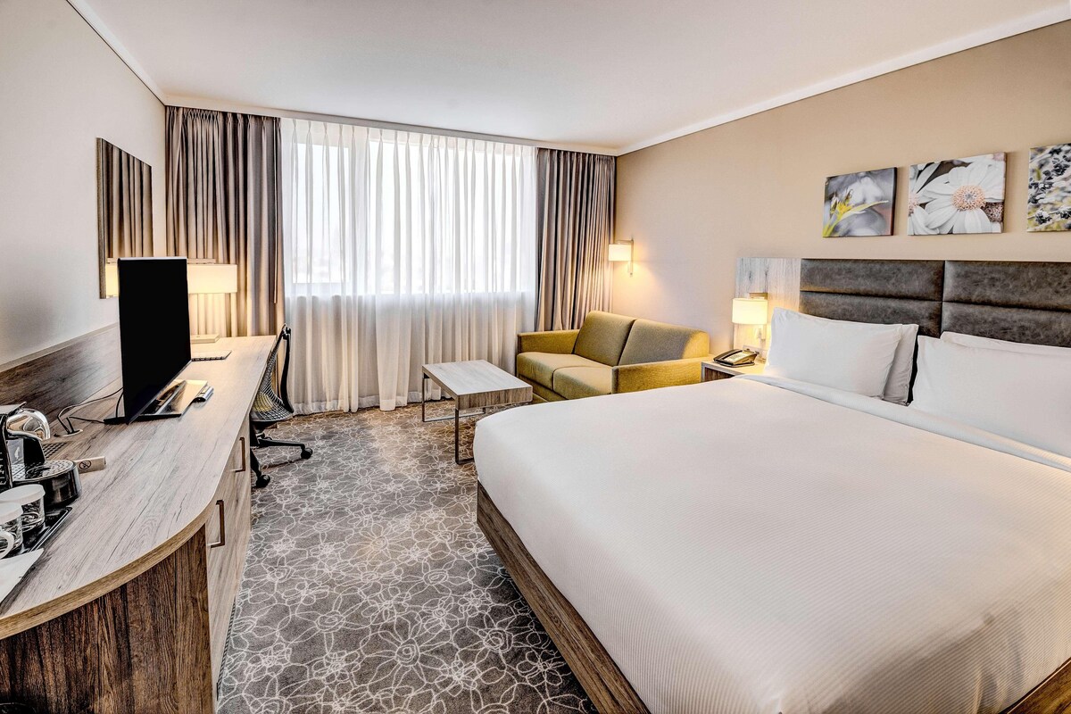 A hotel room with a large bed, a desk with a computer, a chair, and a TV.