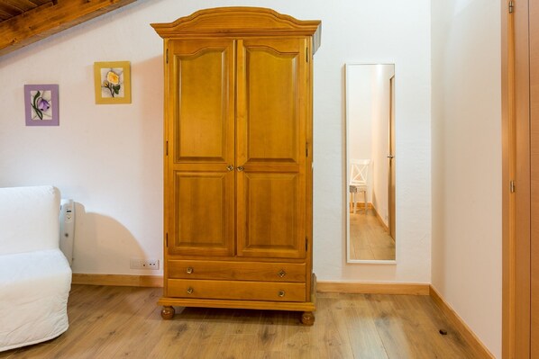 Une chambre avec une armoire en bois, un lit et un miroir au mur.
