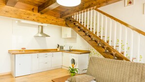 Een compacte keuken met witte kasten, een houten aanrechtblad en een ingebouwde vaatwasser. Een houten trap met witte leuningen leidt naar een hoger gelegen verdieping.