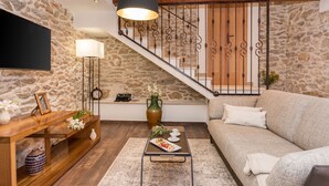 Un salon avec un mur en pierre, un escalier en bois, un canapé, une table basse et un téléviseur.