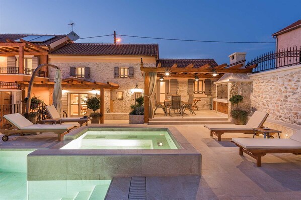 A villa with a swimming pool, outdoor seating, and a stone wall.