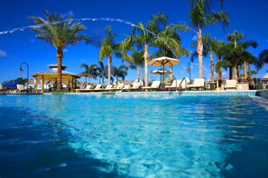 A pool area with clear blue water, surrounded by palm trees and lounge chairs.